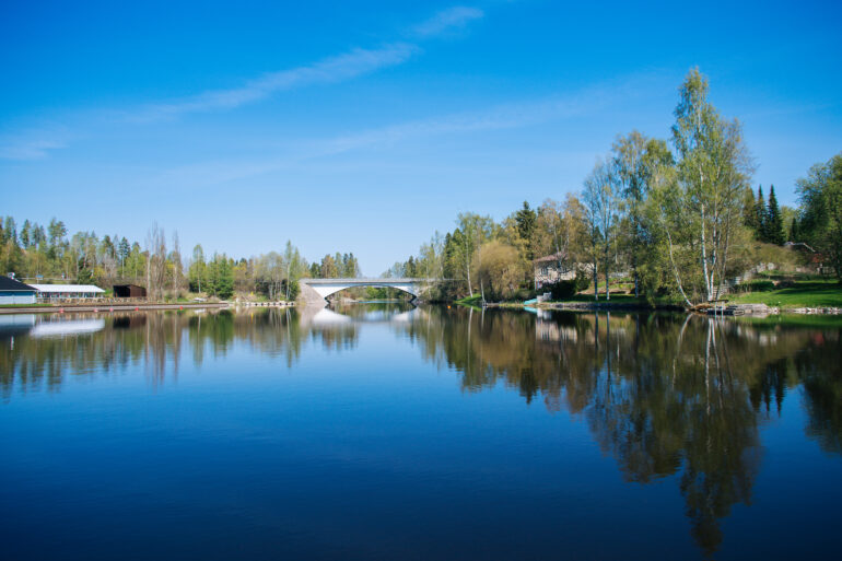 Tyyni joki, jonka päässä näkyy pieni ja vanha silta.