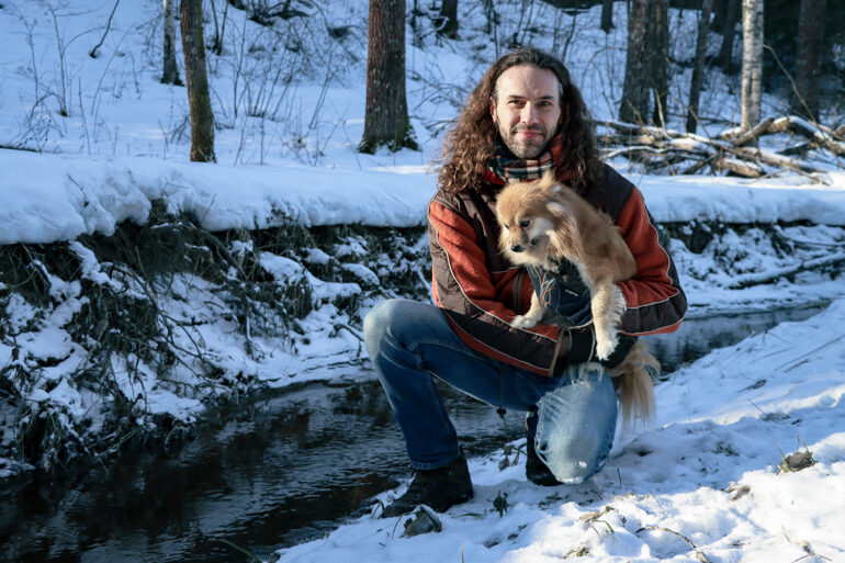 Michel kyykyssä talvisessa metsässä koira sylissään.
