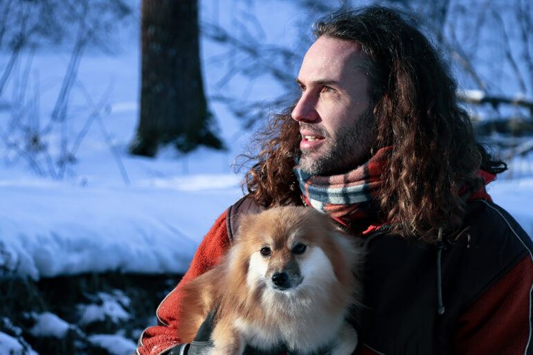 Michel talvisessa metsässä koira sylissään katse suunnattuna metsään.