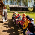 Luokkaretkellä olevat lapset kuuntelevat torpparin asuun pukeutunutta opasta torparimuseon pihamaalla.