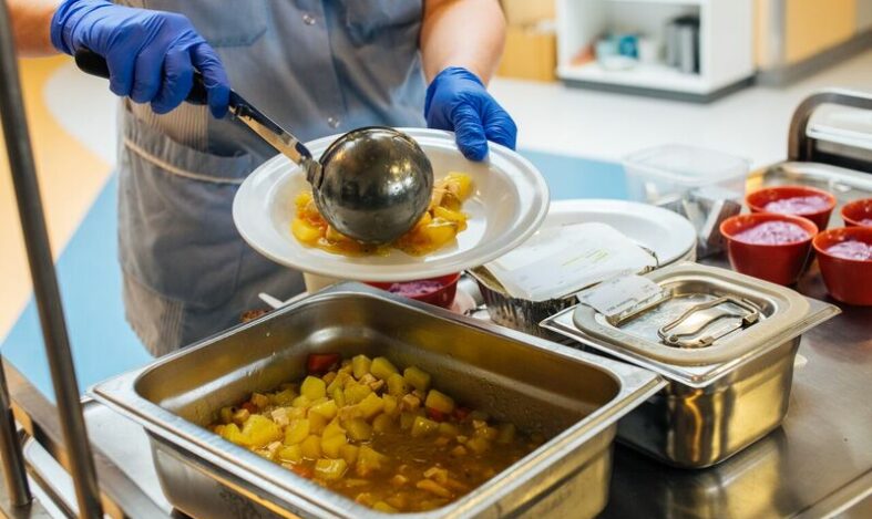 Ateriapalvelujen työntekijä annostelee soppaa lautaselle.