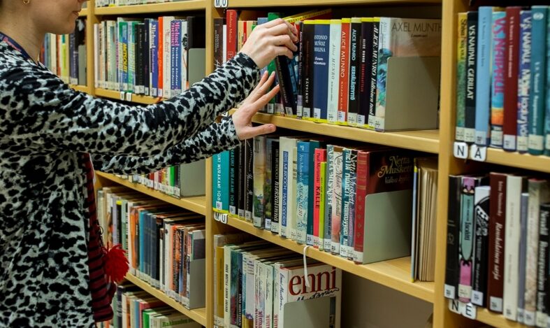 Henkilö ottaa kirjaa kirjahyllystä.