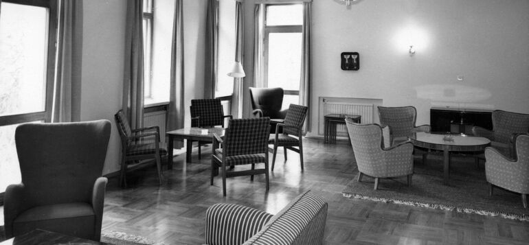 Vanha kuva virkailikerhon sisätiloista. pöytä - ja sohvaryhmineen.