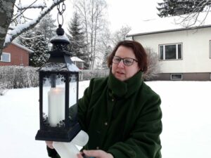 Jutta laittaa kynttilöitä lyhtyihin talvisella kotipihallaan.