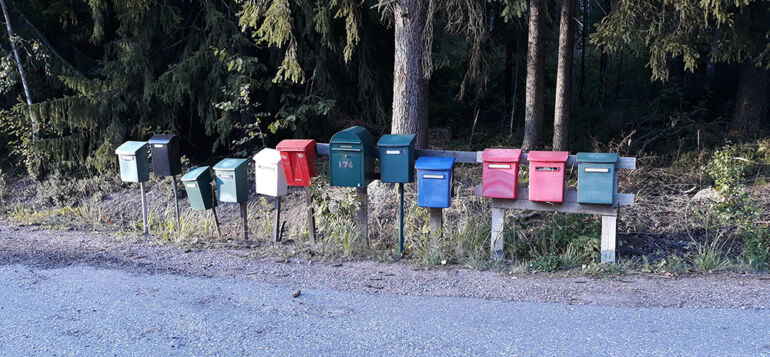 Eriväriset postilaatikot rivissä metsänreunassa.