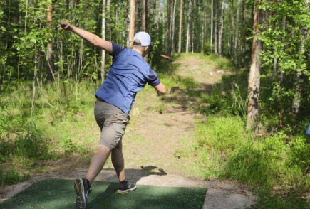 ReTee ry:n talkoileman frisbeegolfradan avajaisissa henkilö heittämässä frisbeetä.