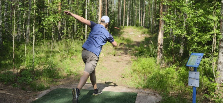 ReTee ry:n talkoileman frisbeegolfradan avajaisissa henkilö heittämässä frisbeetä.