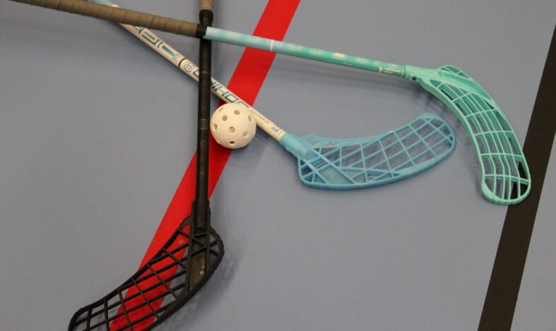 Kolme salibandymailaa ja pallo liikuntasalin lattialla.