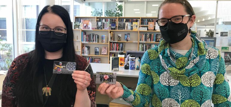 Kaksi kirjaston työntekijää esittelee kädessään lainattavia kausikortteja.