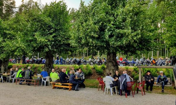 Asiakkaita Mallinkaisten motoristikahvilan pöydissä puiden suojissa.