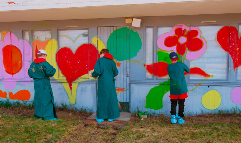 Lapset maalaavat virheissä suojavarusteissaan kukkia ja sydämiä rakennuksen seinälle.