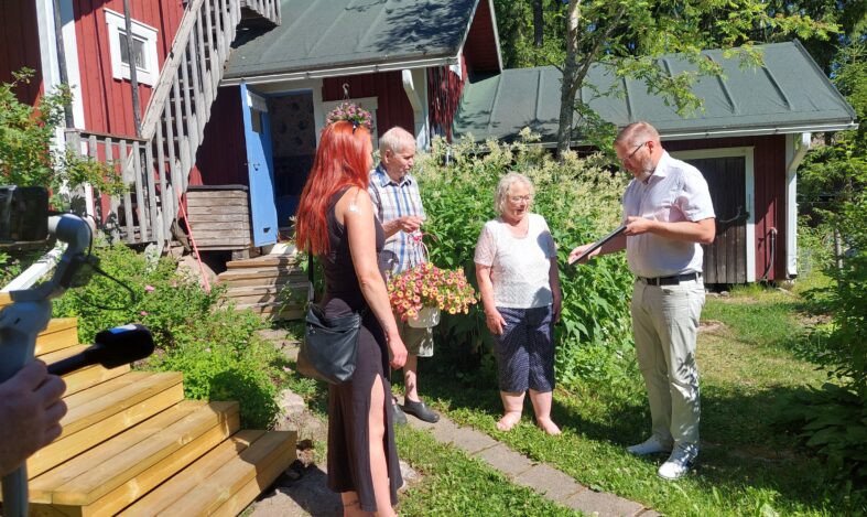 Tuomaristo onnittelee pariskuntaa mökin pihalla.