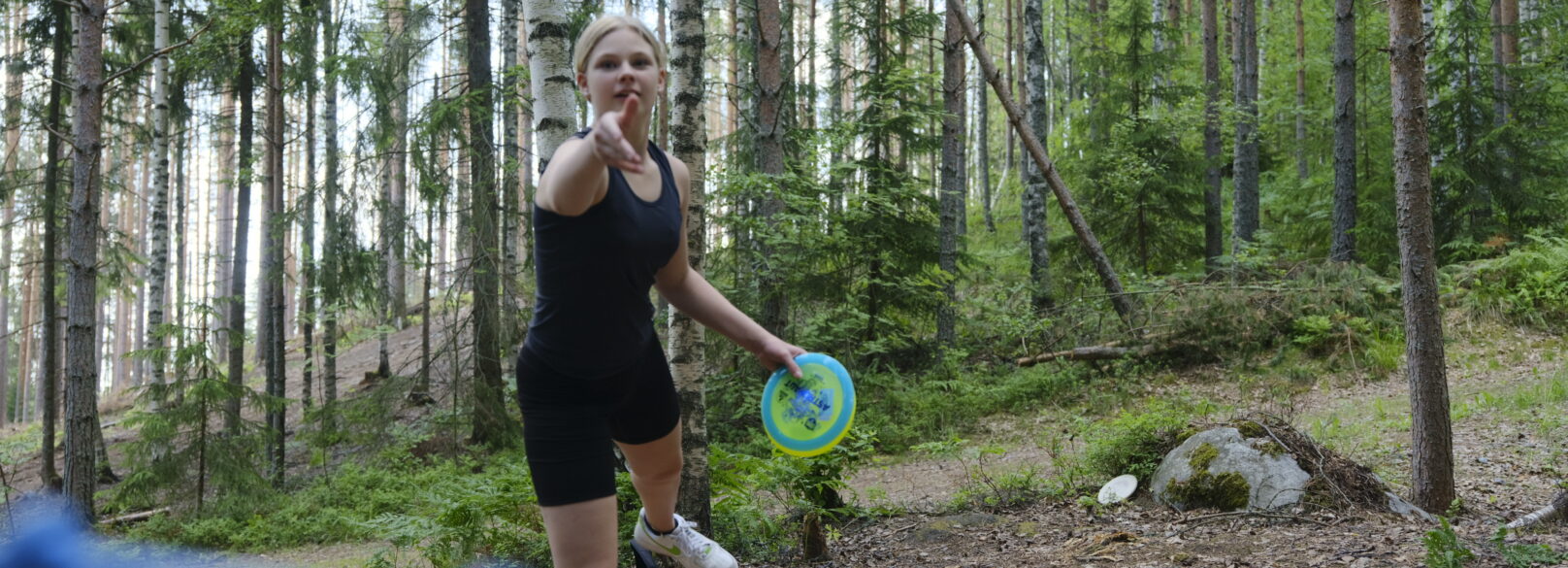 Frsibeekiekkoa heittävä tyttö metsässä.