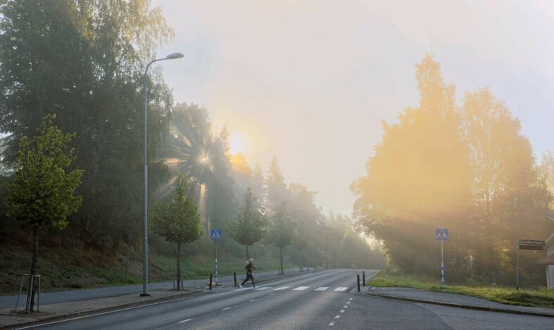 Lenkkeilijä ylittää tien aamusumussa.