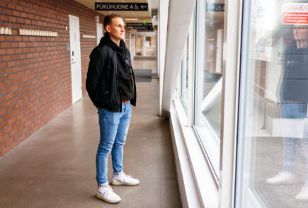 Mies seisoo käytävällä ikkunan edessä ja katsoo ulos ikkunasta.