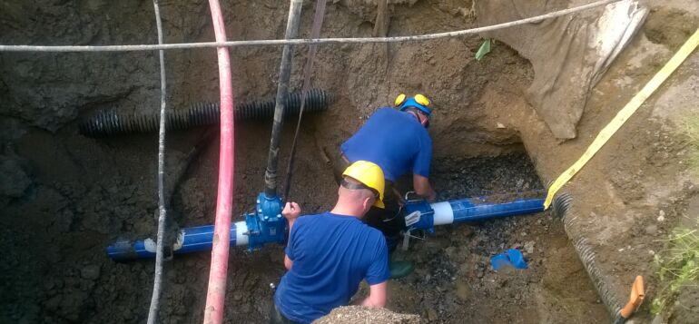 Two people in blue shirts and yellow safety helmets working on a water pipe.