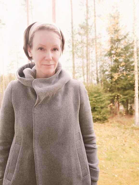 Hyvinvointijohtaja Hanna Paikkala harmaa takki päällä ulkona. Taustalla näkyy nurmikkoa ja puita.