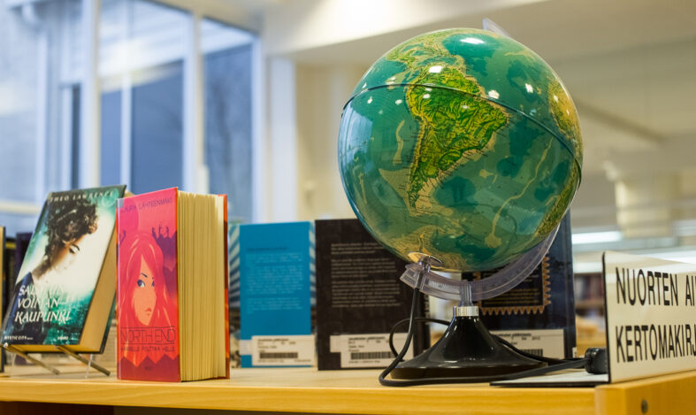 Karttapallo kirjastossa hyllyn päällä, vieressä myös muutama kirja.