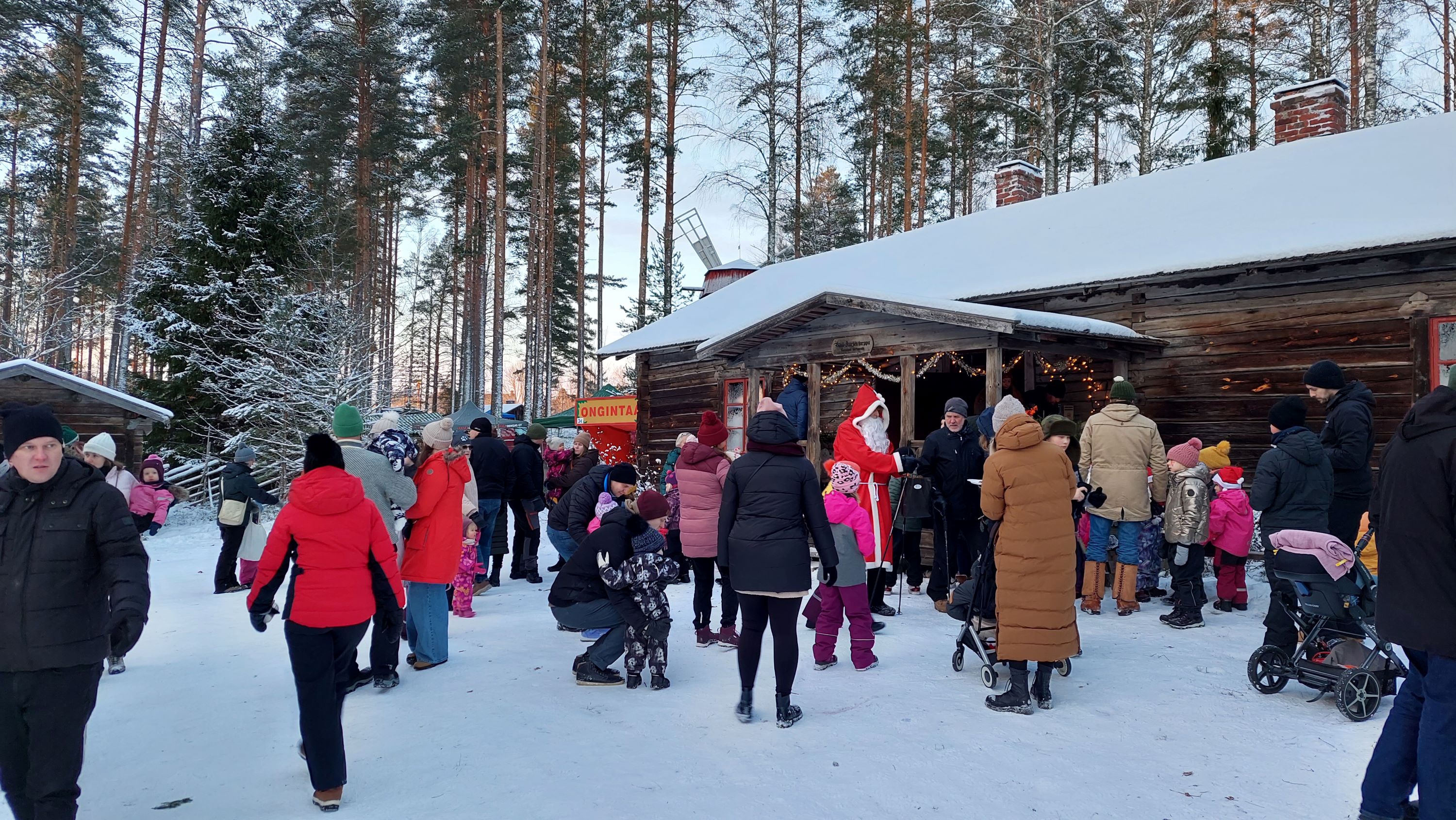 People at the Christmas market in Laurinmäki. People greeting Santa Claus in front of a croft decorated with Christmas lights.